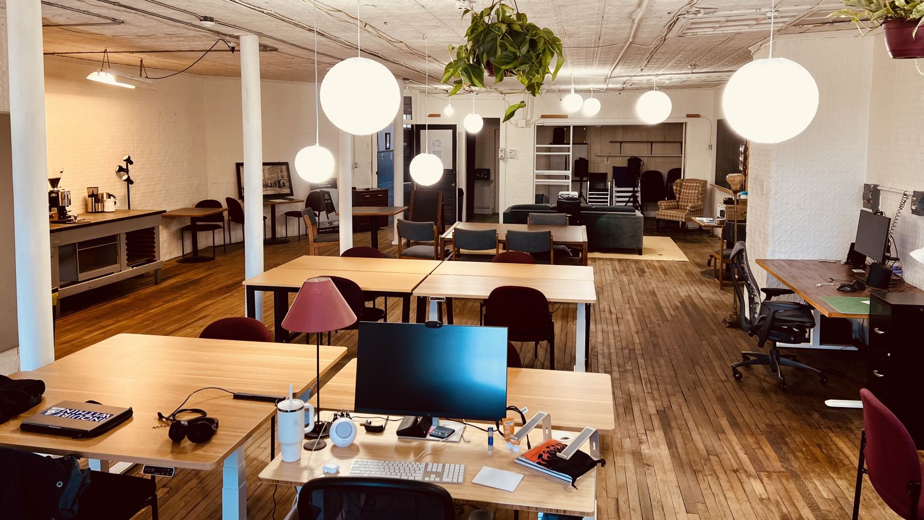 The coworking loft: sit/stand desks, hanging globe lights, and wood floors under a tin ceiling
